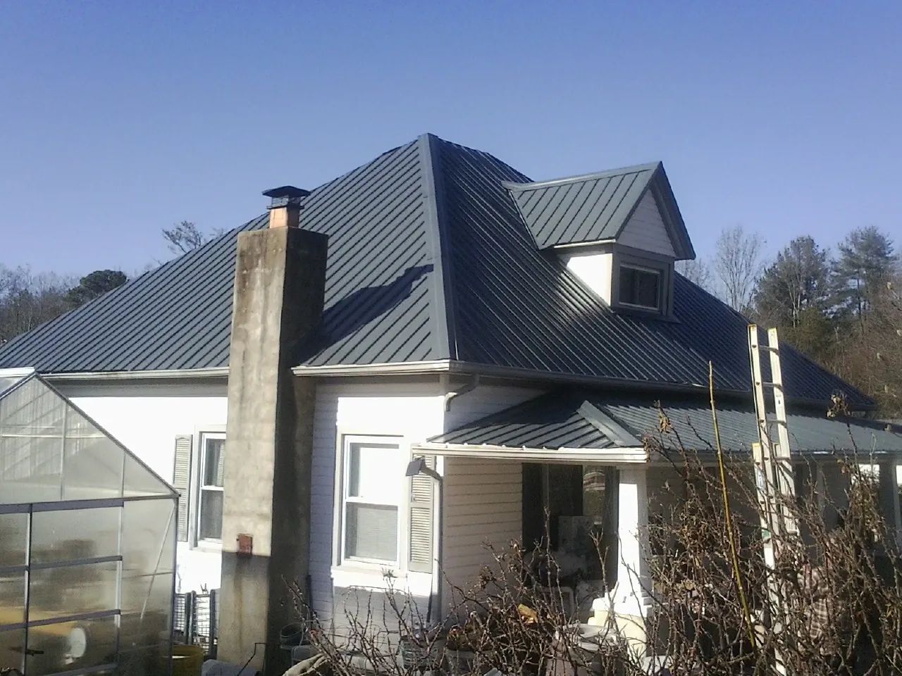 Dark blue standing seam metal roof on a white farmhouse with dormer — Slate & Tile Roof Repair by Roofing Brothers in Oxford Junction
