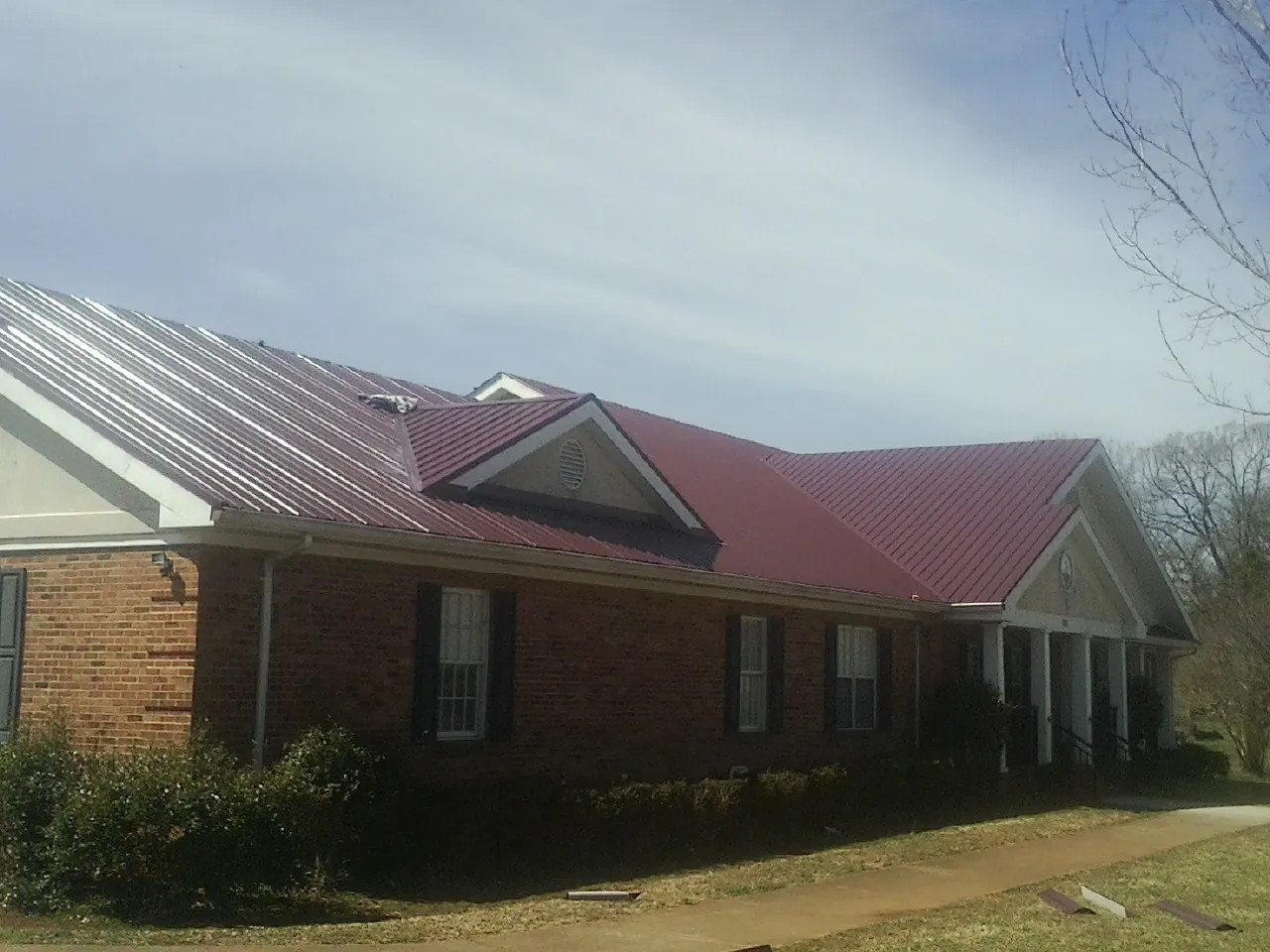 Red metal roof with gabled entries on a long brick building, from a Hail Damage Roof Repair job in Oxford Junction
