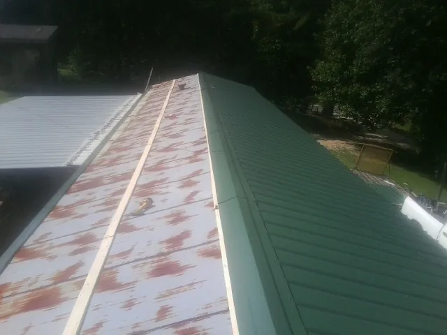 Old rusted panels beside newly installed green metal roofing — Wind Damage Roof Repair by Roofing Brothers in Oxford Junction