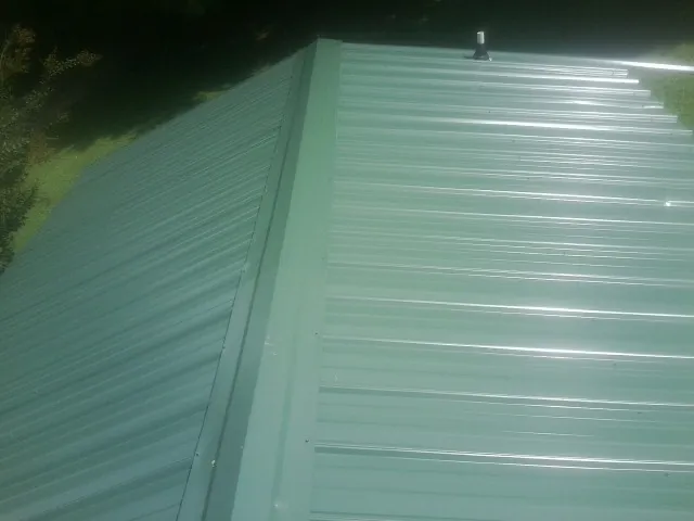 New green metal panels meeting at the ridge of a roof — Flat Roof Repair work by our crew in Oxford Junction