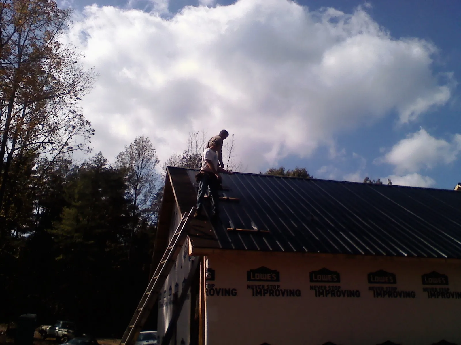 Roofer fastening dark metal panels high against a cloudy sky, from a Roof Inspection job in Oxford Junction