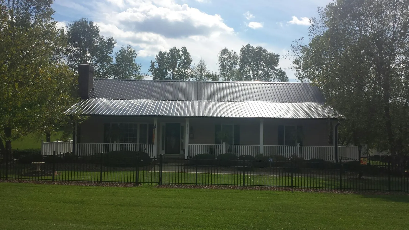 Gray metal roof on a brick ranch with a full width front porch — Gutter Guard Installation work by our crew in Oxford Junction