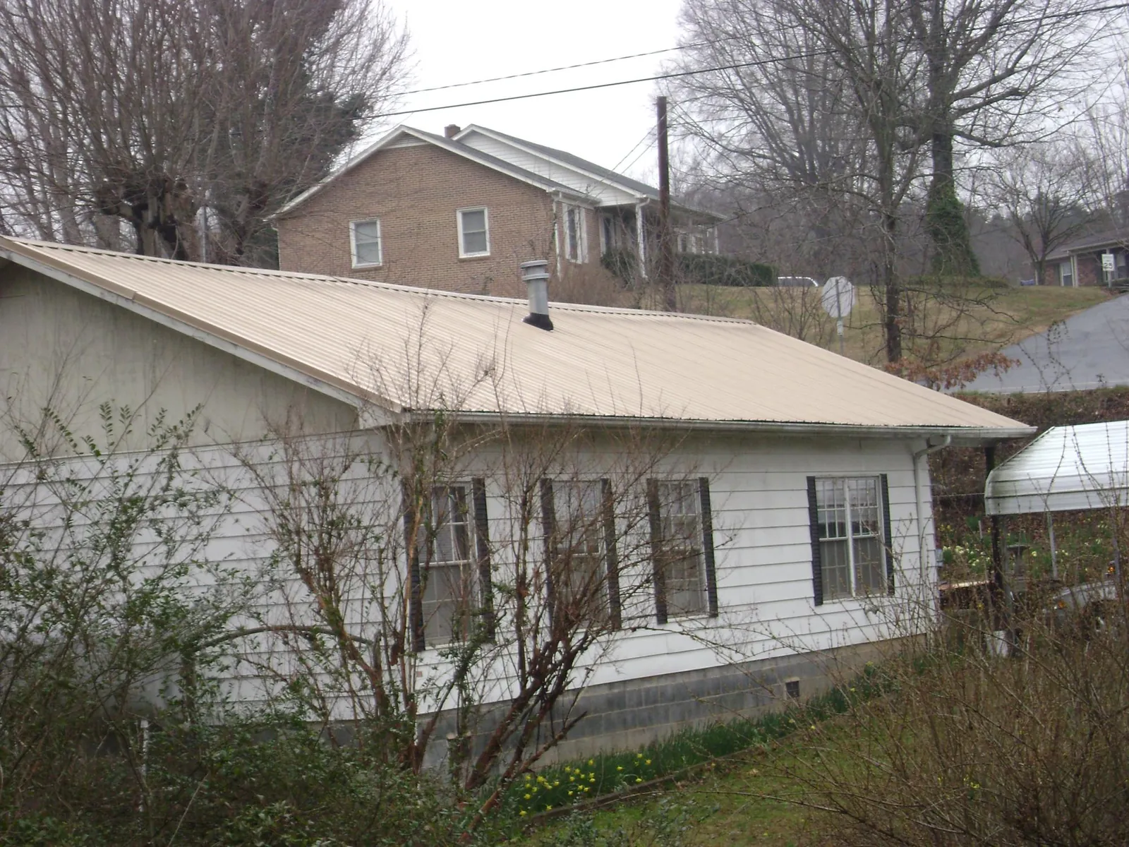 Tan metal roof on a white sided house set into a hillside — Commercial Roofing by Roofing Brothers in Oxford Junction