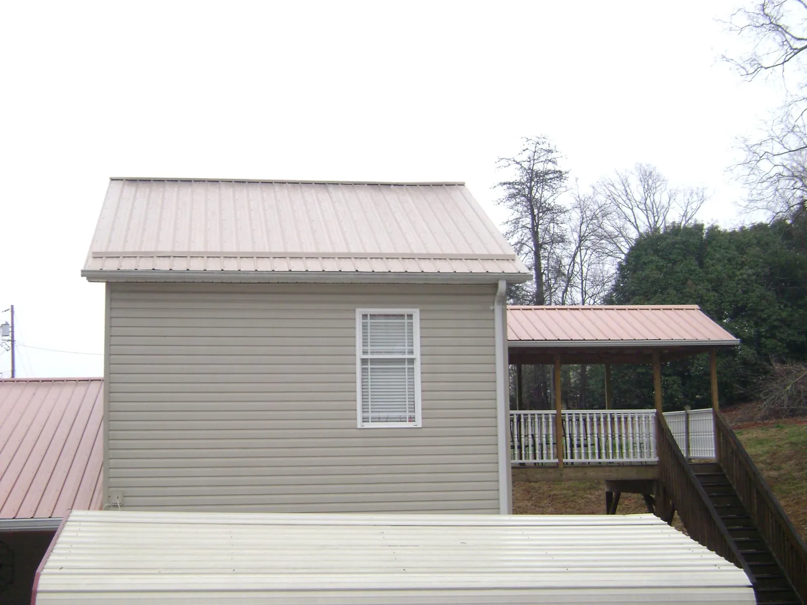 Tan metal roofs on a two story addition and attached porch, from a Roof Replacement job in Oxford Junction