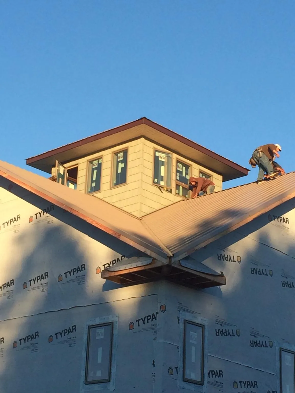 Roofers working around a rooftop cupola on a new metal roof at sunset — Roof Waterproofing in Oxford Junction by Roofing Brothers